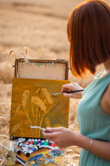 Wall Mural - Back view of a girl painter depicting wheat spikelets on canvas. Young girl doing her favourite hobby