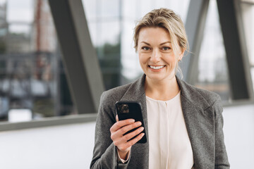 Portrait of a beautiful mature business woman in suit and gray jacket smiling and talking on the phone on the modern urban background