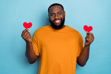 Wall Mural - Portrait of attractive cheerful guy holding two small little hearts romance isolated over bright blue color background