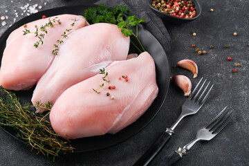 Wall Mural - Chicken breast. Raw chicken breast fillets on black ceramic plate on wooden cutting board with herbs and spices on black background. Top view with copy space.