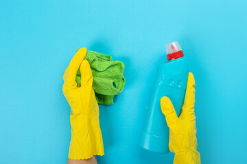 The hands of a housewife in yellow rubber protective gloves hold a bottle of household chemicals and a rag. Detergent for various surfaces in the kitchen, bathroom and other rooms. 