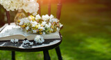 Fototapeta Fototapeta w kwiaty na ścianę - książka, wianek i bukiet białego bzu jako kompozycja na starym krześle w słonecznym ogrodzie