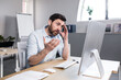 © Liubomir - Annoyed, emotional, nervous young man, office worker, manager talking on a video call at the computer, sitting at a table in the office in white clothes