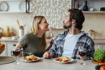 Glad happy handsome caucasian millennial couple eat pasta together, have fun in light kitchen interior, profile