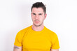 © Roquillo - Displeased Young caucasian man wearing yellow t-shirt over white background frowns face feels unhappy has some problems. Negative emotions and feelings concept