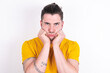 © Roquillo - Portrait of sad Young caucasian man wearing yellow t-shirt over white background hands face