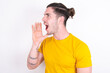 © Roquillo - Young caucasian man wearing yellow t-shirt over white background look empty space holding hand near her face and screaming or calling someone.