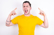 © Roquillo - Photo of crazy Young caucasian man wearing yellow t-shirt over white background screaming and pointing with fingers at hair closed eyes