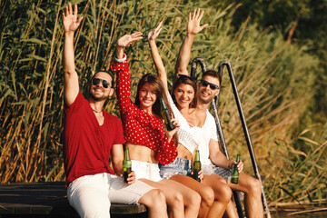 Wall Mural - Happy group of young people drinking beer on a dock by the river during the summer sunny day