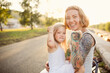 Mom hugs and holds her daughter in her arms, funny emotional mom and daughter show fists at the camera, hipster mom with a tattoo and blonde daughter summer