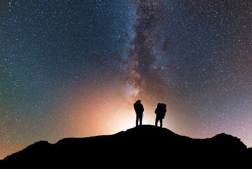 Wall Mural - silhouette of two traveler on the hill in starry night sky. bright milky way galaxy behind him.