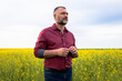 Middle age farmer standing in rapeseed field examining crop.