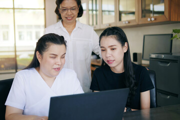 asian women co-workers in workplace including person with blindness disability using laptop computer
