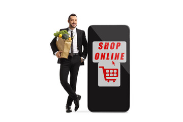 Sticker - Full length portrait of a businessman with a grocery bag leaning on a smartphone with sign for online shopping