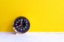 Vintage Antique Wind Up Alarm Clock On A White Table With A Bright Yellow Background