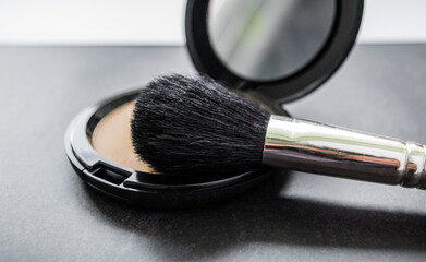 Sticker - A black makeup brush next to an open box with a mirror and powder puff and pink powder. Black background