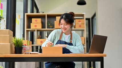 Wall Mural - Female small business owner is writing customer's address and attaching it to a cardboard box