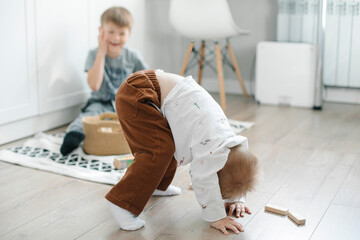 Wall Mural - Children play on the floor of the children's room. Little brother amuses his brother and sister stands on his head at home. Family lifestyle concept