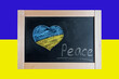 Flag of Ukraine and a heart drawn in chalk. Children write the text Peace on the blackboard with chalk.