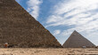 The Great Pyramids of Giza: Cheops and Chephren against a background of blue sky and clouds. The ancient masonry of the nearest one is visible. A horse harnessed to a cart is standing on stony ground.