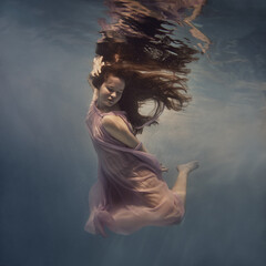 Wall Mural - A girl in a dress with long hair swims underwater as if in zero gravity