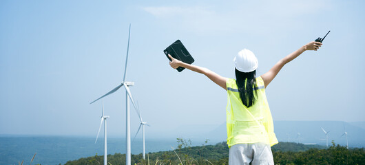 Wall Mural - Beautiful Asian woman Engineer in white helmet working with digital tablet at renewable energy farm. Female inspector controlling functioning of wind turbines .Enery sustainable generator,electricity.