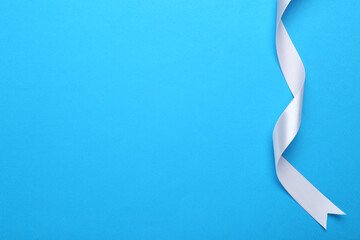 Beautiful white ribbon on light blue background, top view. Space for text