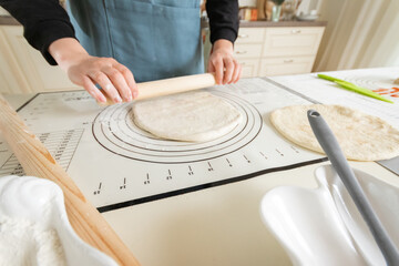 A woman rolls out dough on a silicone baking mat with markings.