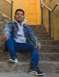 © anuatmoralesfoto - low angle shot of a cool guy with indigenous features looking down at the camera while is sitting on a steps of a neighborhood