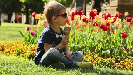 Poster - Cute toddler child, eating ice cream outdoors in the park, spring flowers around him, fountain in garden