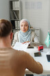 © AnnaStills - Modern Muslim woman working in embassy sitting at desk in front of man passing him documents after approving visa