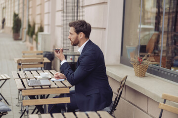 Wall Mural - Caucasian handsome elegant man in cafe outside with laptop, sending voice message. Audio chat.