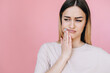 Girl suffering from toothache frowns her face and looks away on a pink background
