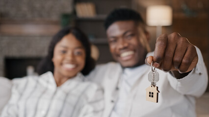 Blurred unfocused view African American married couple newlyweds wife and husband holding keys to new house rented apartment happy with real estate. Girlfriend and boyfriend satisfied living together