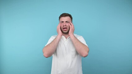 Wall Mural - Shocked bearded man in white t-shirt looking at camera with surprised face isolated on blue background