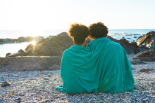 Rear View Of Young African American Couple Wrapped In Blanket Looking At Sea During Sunset