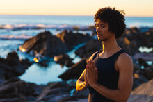 Young African American Man With Eyes Closed, Hands Clasped Practicing Yoga At Beach During Sunset