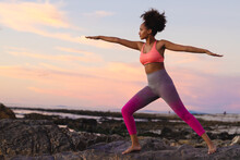 Young Afro African American Woman With Arms Outstretched Exercising At Beach During Sunset