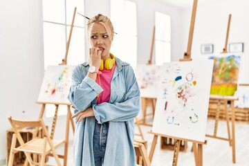 Canvas Print - Young caucasian girl at art studio looking stressed and nervous with hands on mouth biting nails. anxiety problem.