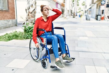 Canvas Print - Young brunette woman sitting on wheelchair outdoors stressed and frustrated with hand on head, surprised and angry face