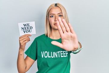 Sticker - Beautiful blonde woman wearing volunteer t shirt showing we need you banner with open hand doing stop sign with serious and confident expression, defense gesture