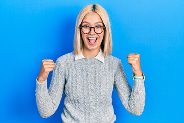 Sticker - Beautiful blonde woman wearing glasses celebrating surprised and amazed for success with arms raised and open eyes. winner concept.