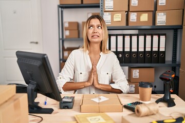 Wall Mural - Young blonde woman working at small business ecommerce begging and praying with hands together with hope expression on face very emotional and worried. begging.