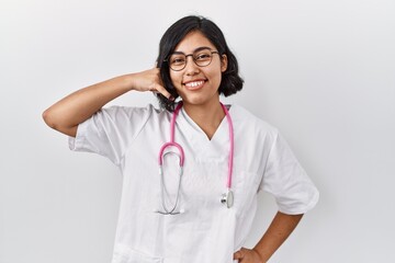 Canvas Print - Young hispanic doctor woman wearing stethoscope over isolated background smiling doing phone gesture with hand and fingers like talking on the telephone. communicating concepts.