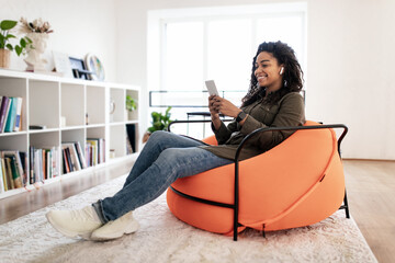 Canvas Print - Smiling black woman in wireless headhones using cell phone