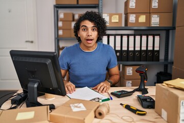 Poster - Hispanic man with curly hair working at small business ecommerce afraid and shocked with surprise and amazed expression, fear and excited face.