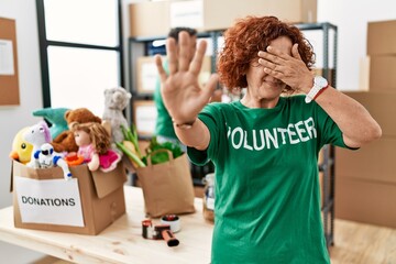 Poster - Middle age woman wearing volunteer t shirt at donations stand covering eyes with hands and doing stop gesture with sad and fear expression. embarrassed and negative concept.