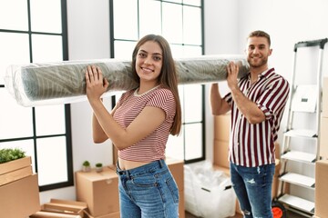 Sticker - Young caucasian couple smiling happy holding carpet at new home.