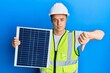 © Krakenimages.com - Handsome young man holding photovoltaic solar panel with angry face, negative sign showing dislike with thumbs down, rejection concept