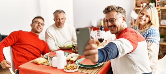 Poster - Group of middle age friends smiling happy having christmas dinner and making selfie by the smartphone at home.